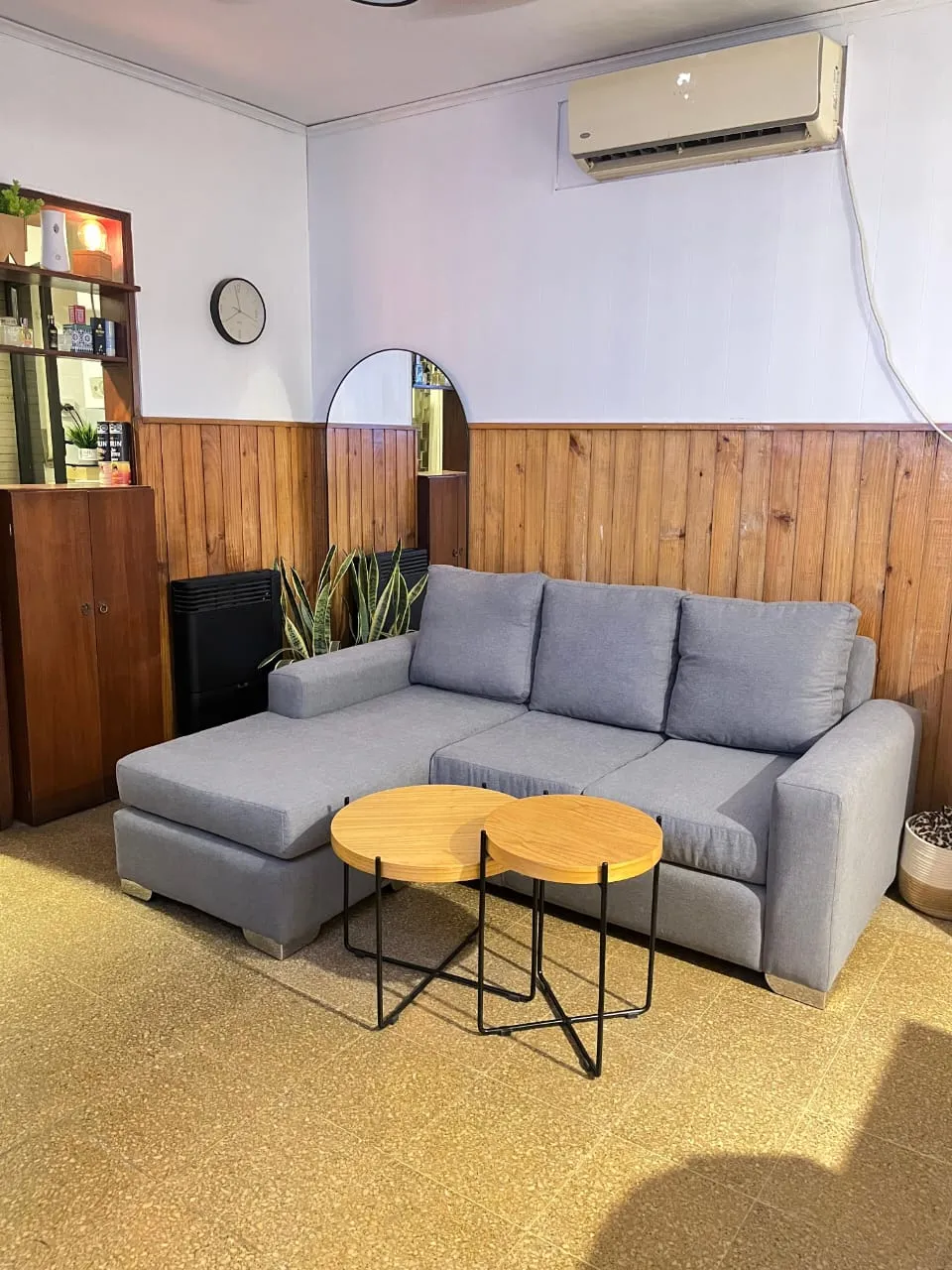 Sillón esquinero en tela gris claro, con mesas ratonas redondas delante